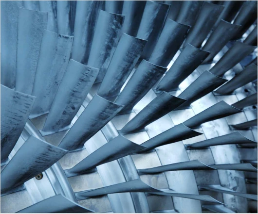 Close-up of metallic turbine blades arranged in a circular pattern, showcasing an industrial, mechanical design with a blue tint. This intricate display represents the cutting-edge of turbomachinery development, highlighting new strides in commercialization services.